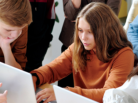 Female student using laptop surrounded by classmates