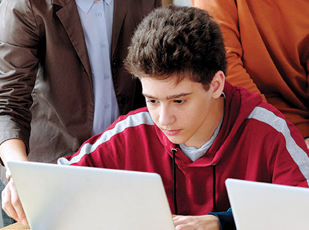 Male student using laptop surrounded by classmates